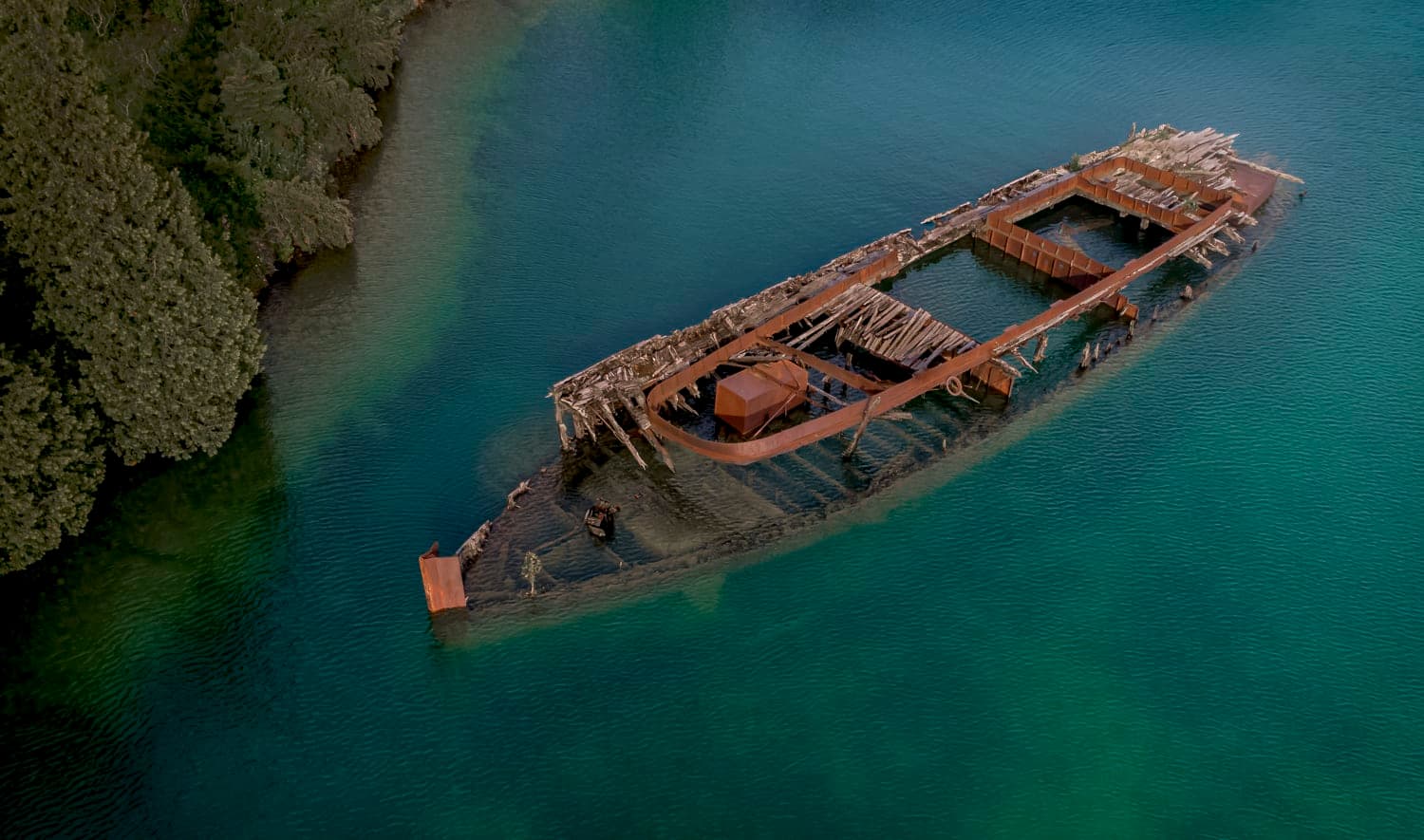 A wrecked ship's frame resting in clear shallow water