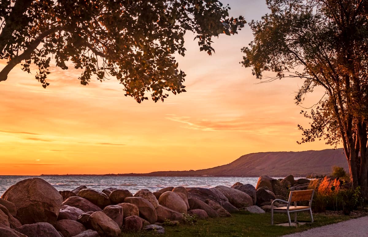 Empty bench above the shoreline boulders as the sun sets behind the escarpment