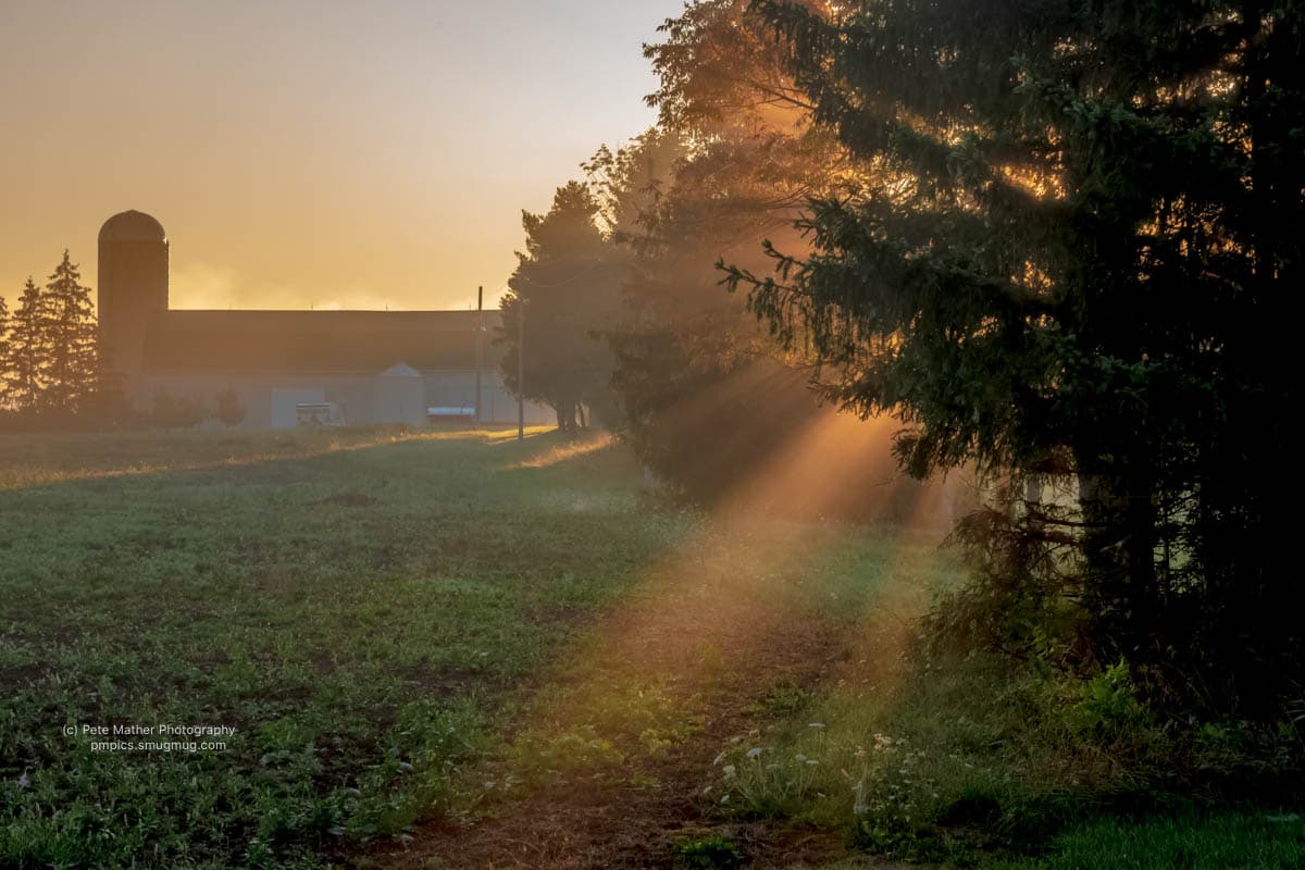 Barn and silo beside a misty field with rays of light