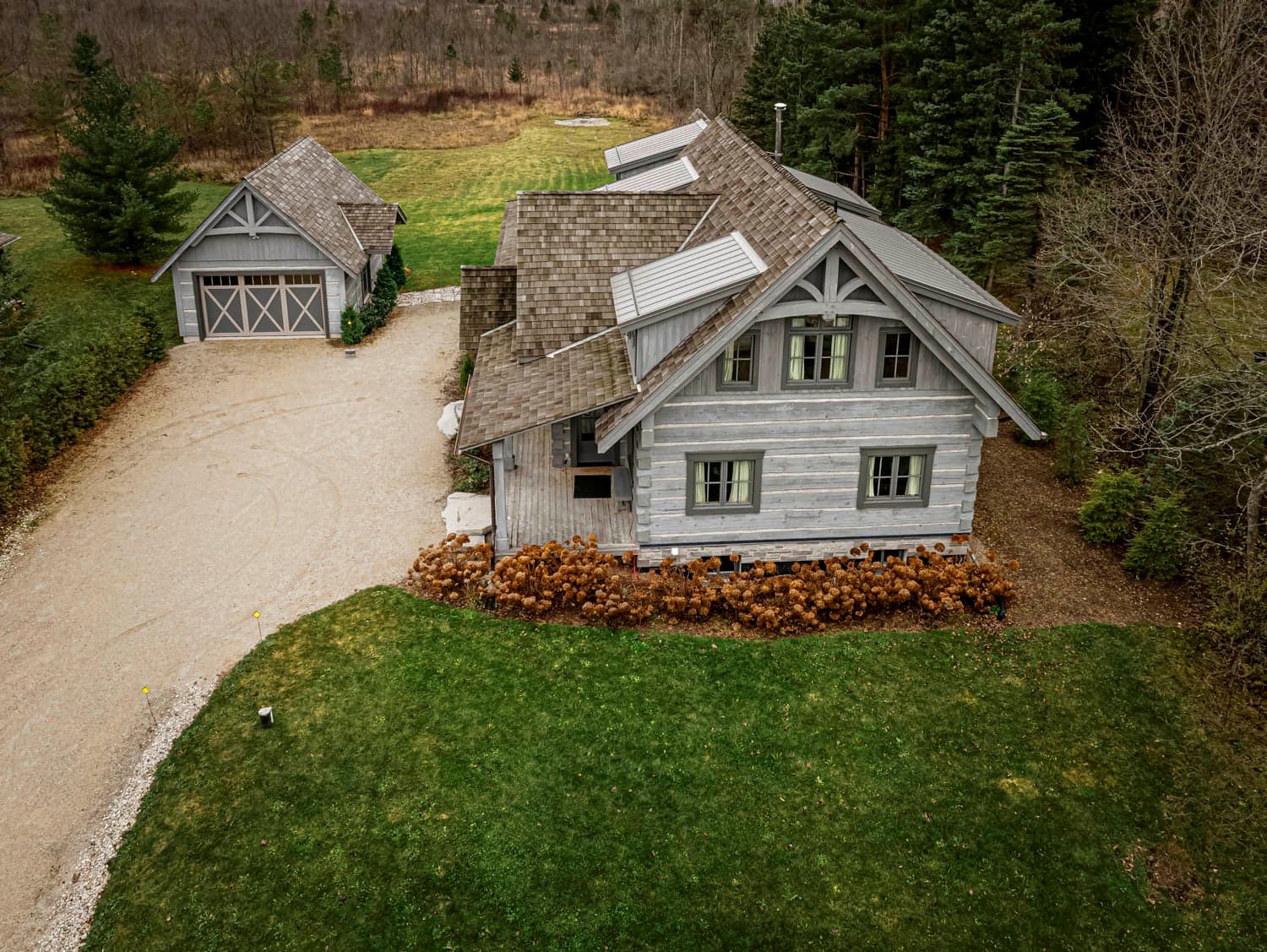Timber-frame chalet home and detached garage above a gravel drive